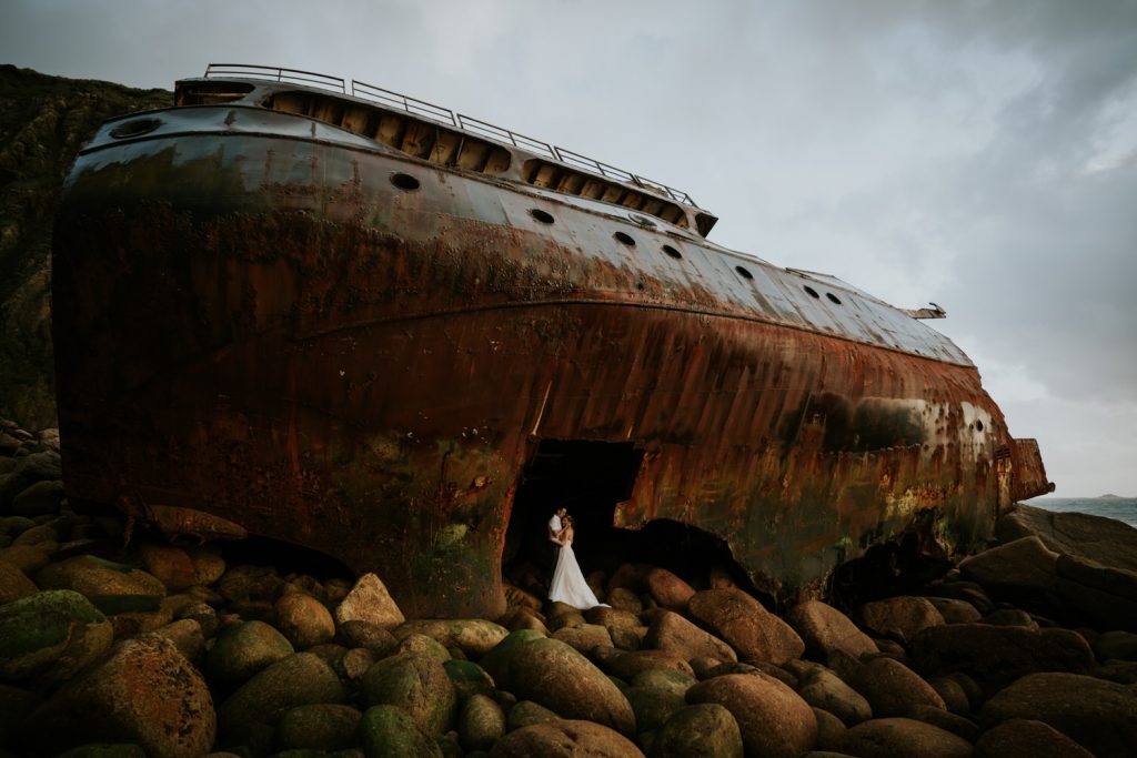 A bride and groom kiss and hug inside the broken hull of the shipwreck at Sennen Cove on their elopement 