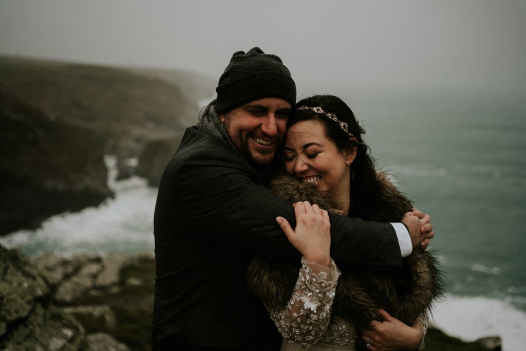 A elopement couple hold each other tightly as the rain hits their faces on their outdoor winter elopement in Cornwall 