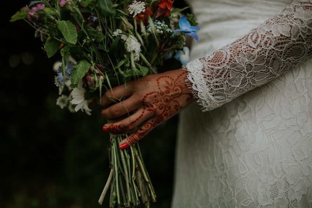 A pagan wedding bride holds her wild bouquet with henna on her hands 