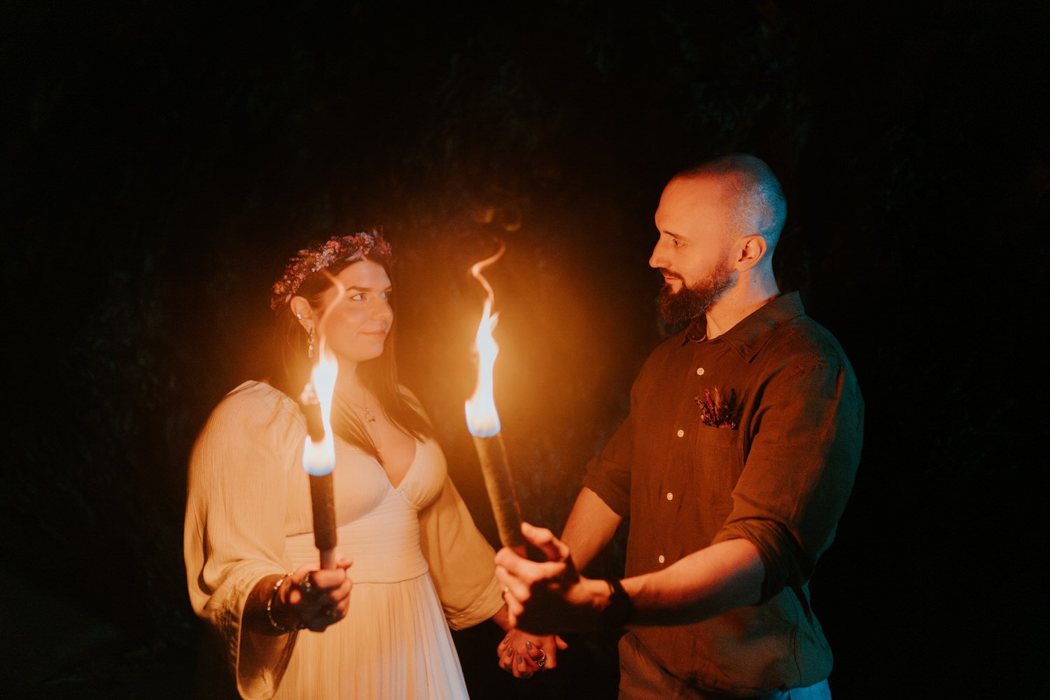 Moody and atmospheric sea cave elopement ceremony with couple holding fire torches for pagan handfasting ceremony